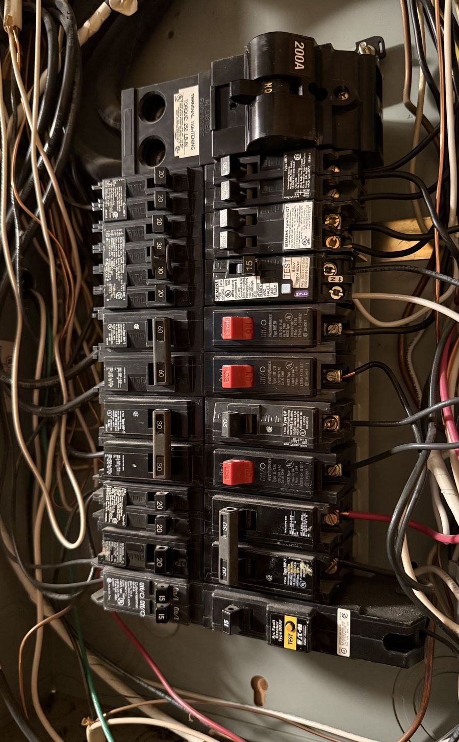 Older electrical panel with mixed breaker brands and crowded wiring behind the cover