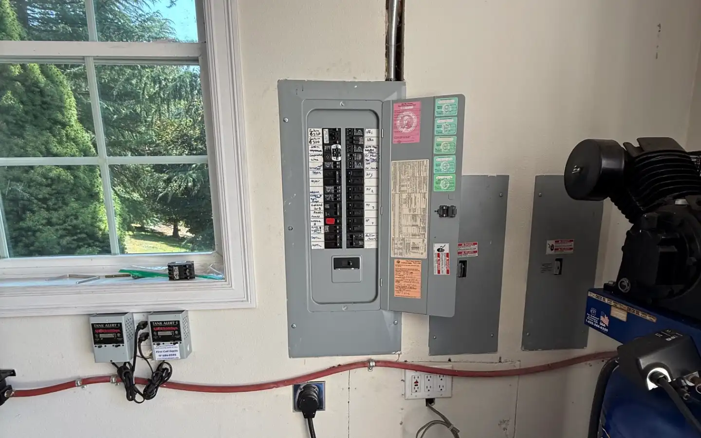 Garage electrical panel beside a window, with a large plug-in connection on the wall below it