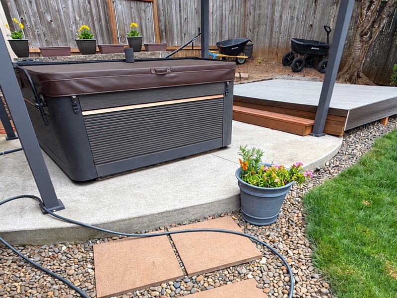 Covered hot tub on a concrete pad in a fenced backyard
